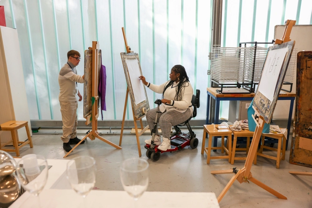Woman in wheelchair and man with Down Syndrome painting in creative workshop during art classes