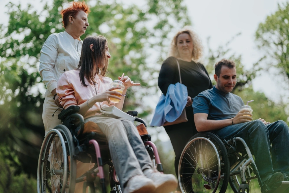 two disabled individuals on wheelchair in a park with two carers