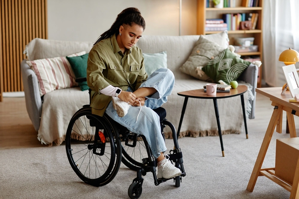 women sitting on wheel chair in her home and tying shoe laces